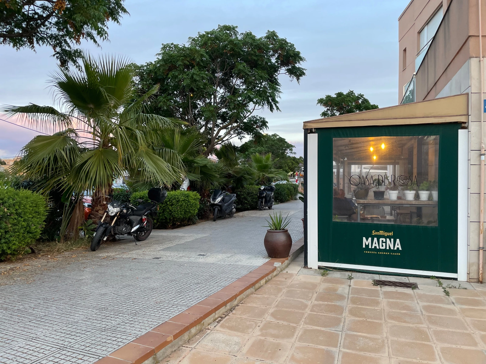 Aproximación exterior con cartel iluminado, borde de terraza, vegetación y paseo