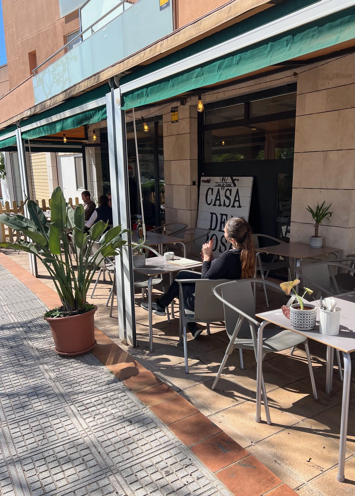 Fachada y terraza exterior con cartel, toldo y plantas en macetero