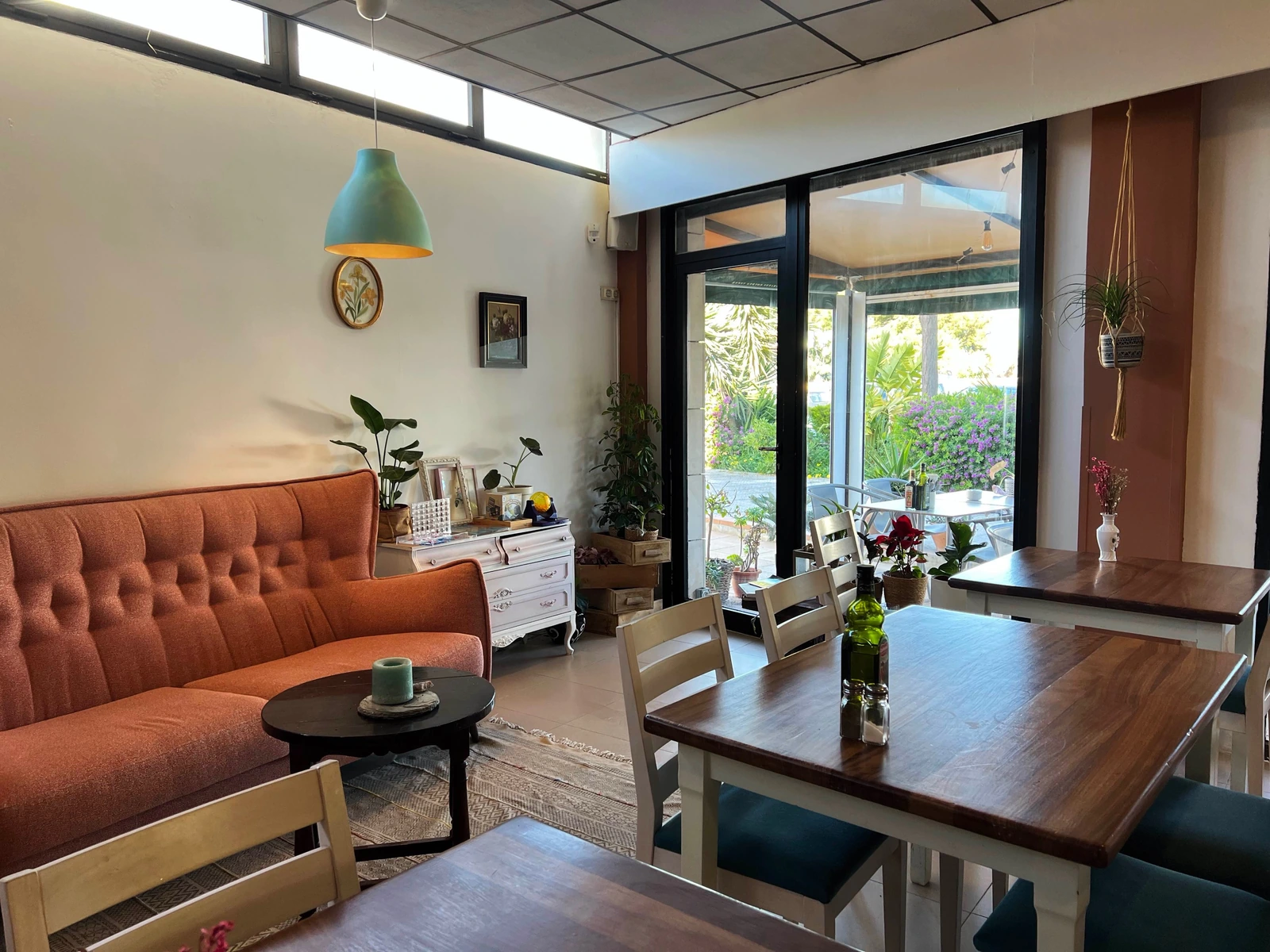 Rincón cálido con banco tapizado, mesas bajas, plantas y luz de terraza