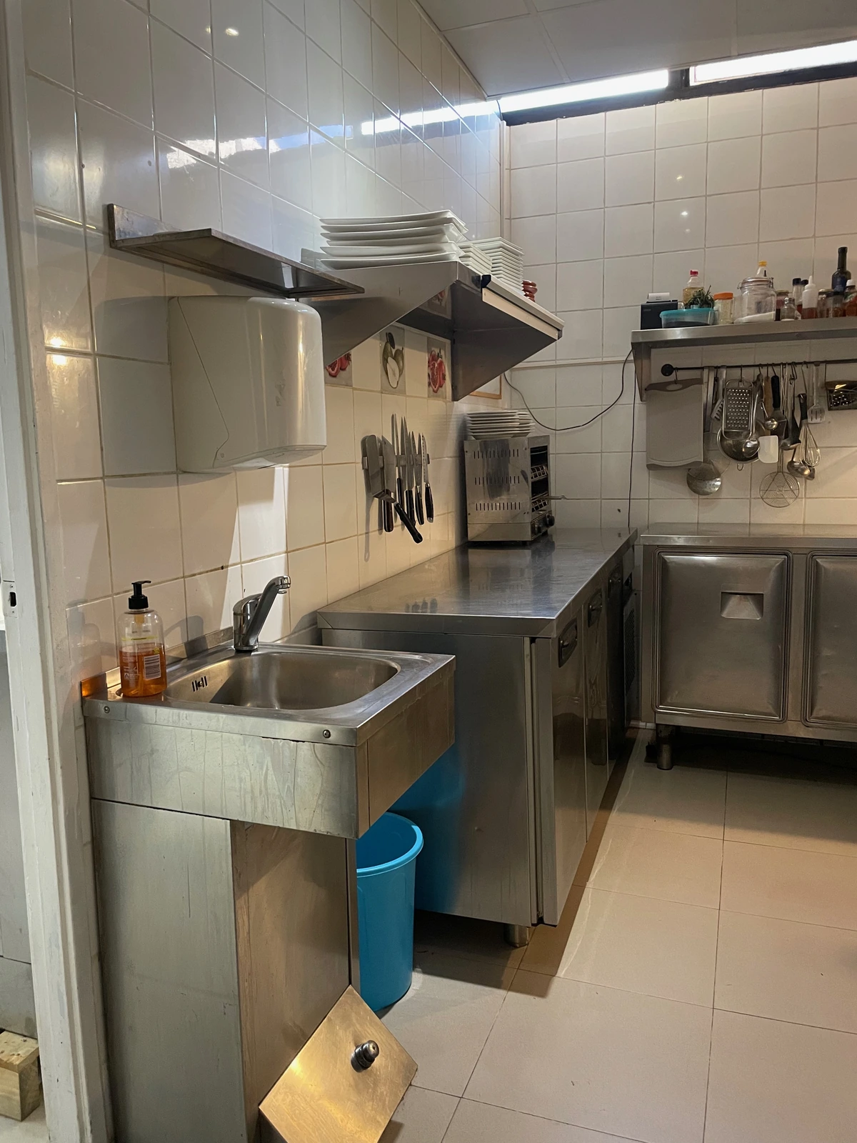 Fregadero y zona de prep en acero inoxidable con cuchillos y estanterías al muro