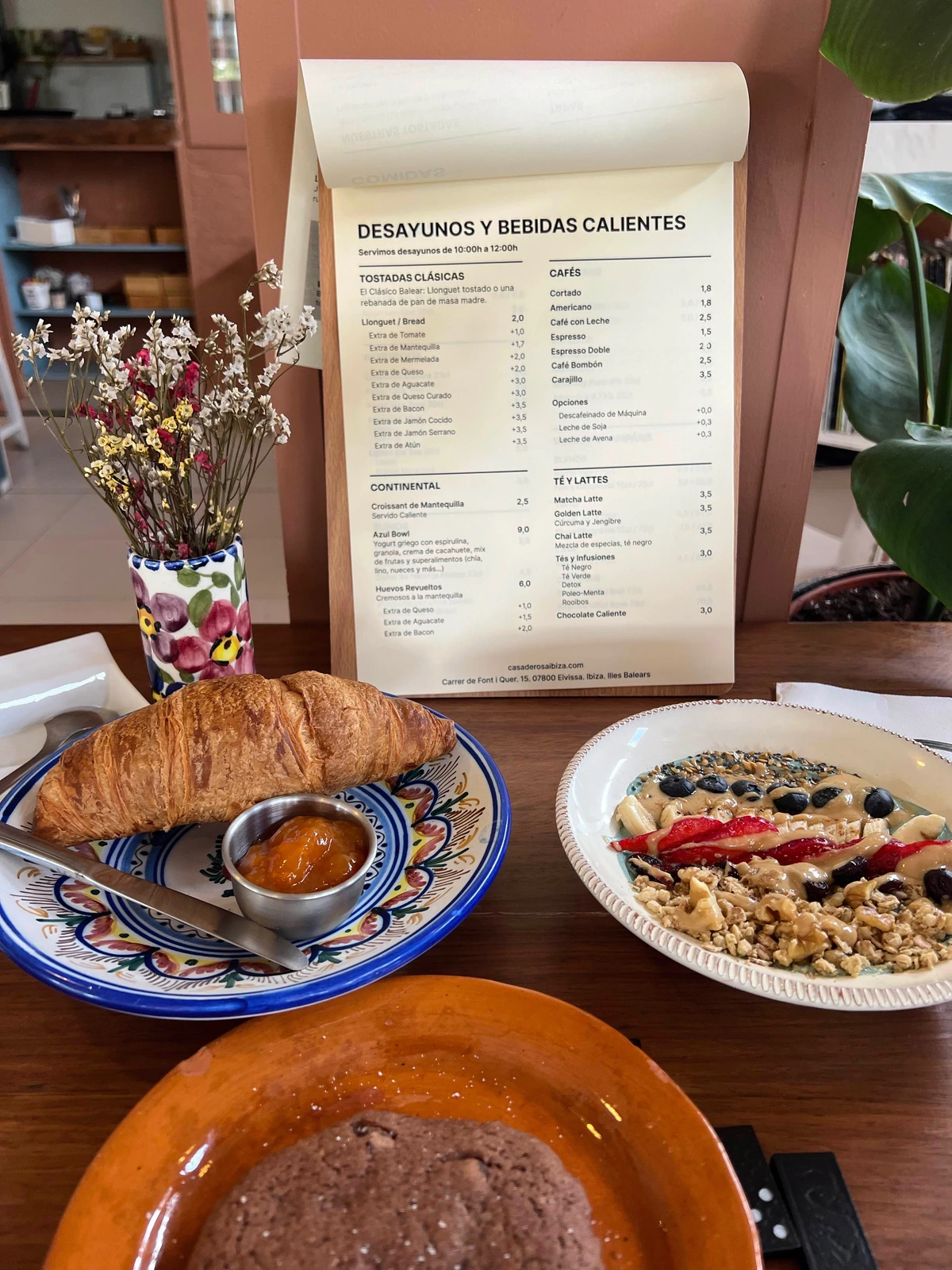 Desayuno con marca: croissant, bowl, bebida caliente y pizarra del menú detrás