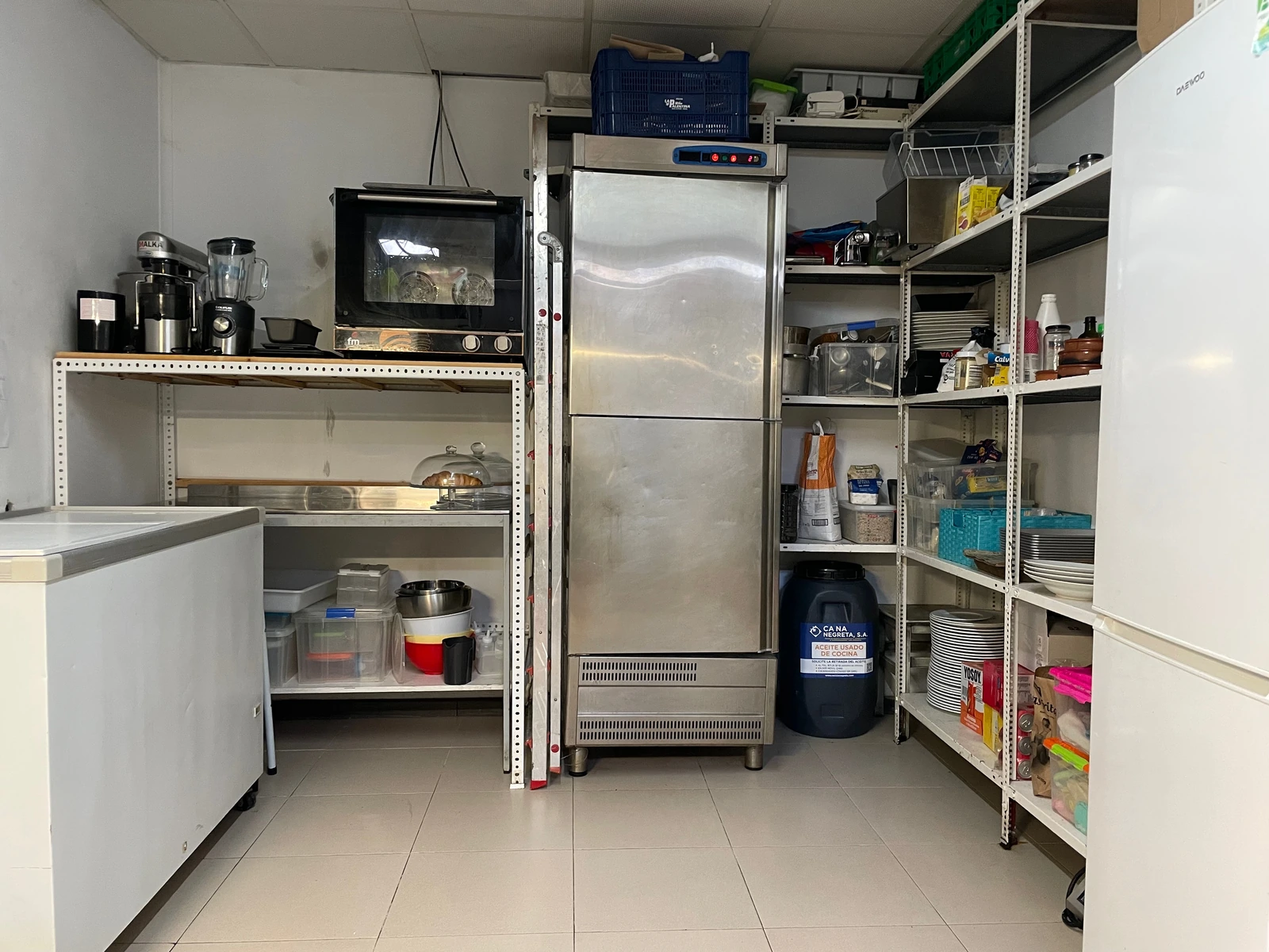 Almacén con frigorífico vertical, estantes, congelador, horno y suministros