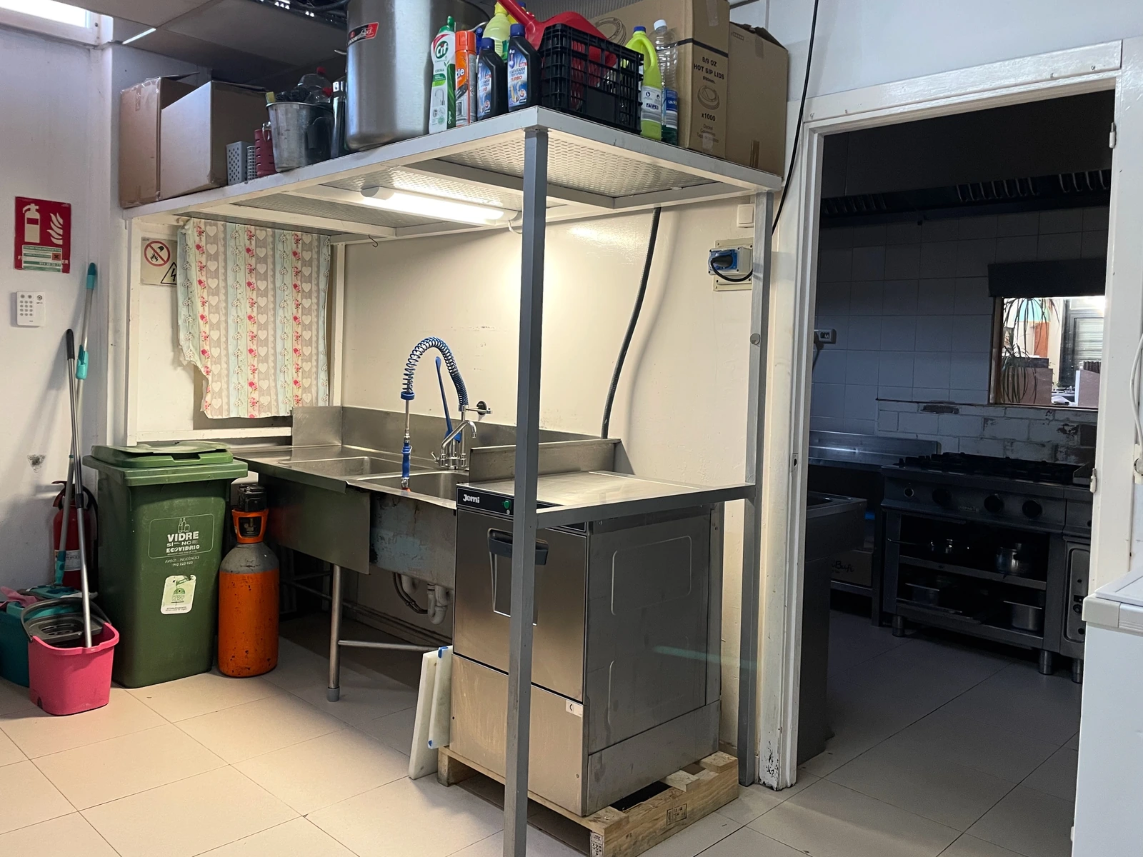 Fregadero de acero, zona de prep, entrada al almacén y útiles de limpieza