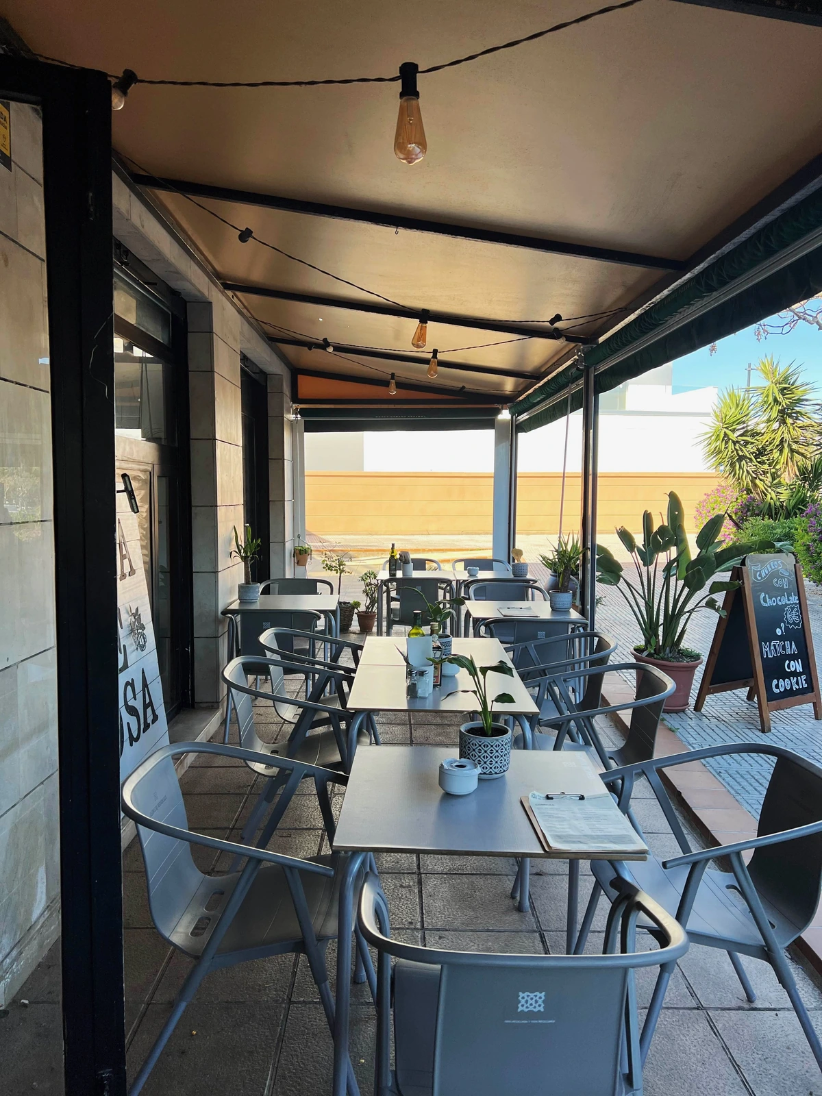 Terraza cubierta con mesas metálicas, sillas, toldo y plantas